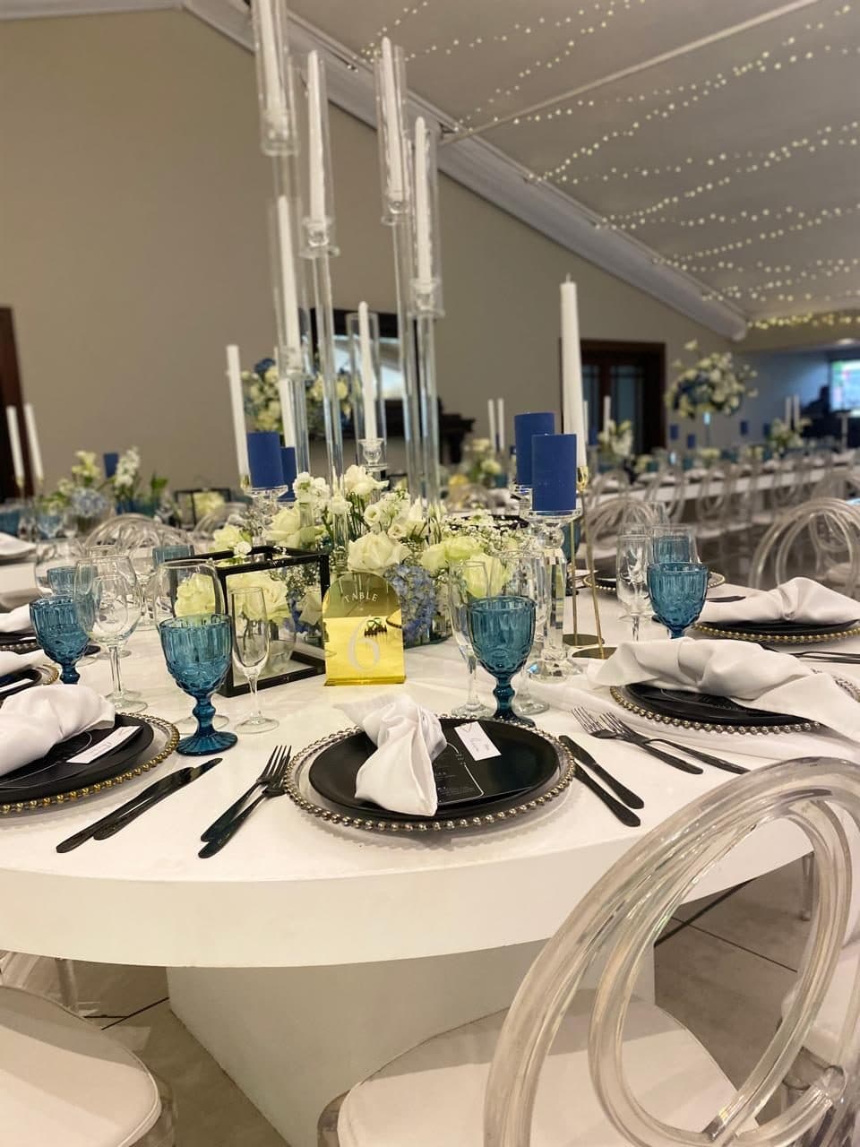 Round guest table with blue goblets, black chargers and a gold table number