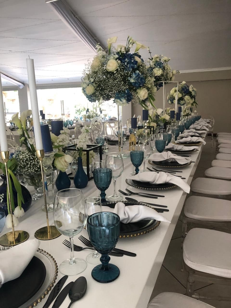 Long banquet table dressed in blue and white with raised floral centrepieces