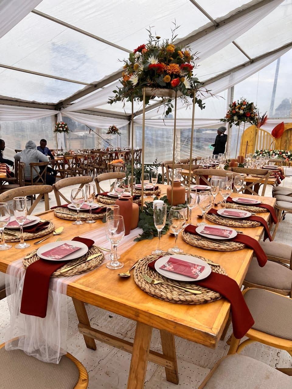 Clear-roofed marquee with wooden tables, terracotta vases and raised autumn florals