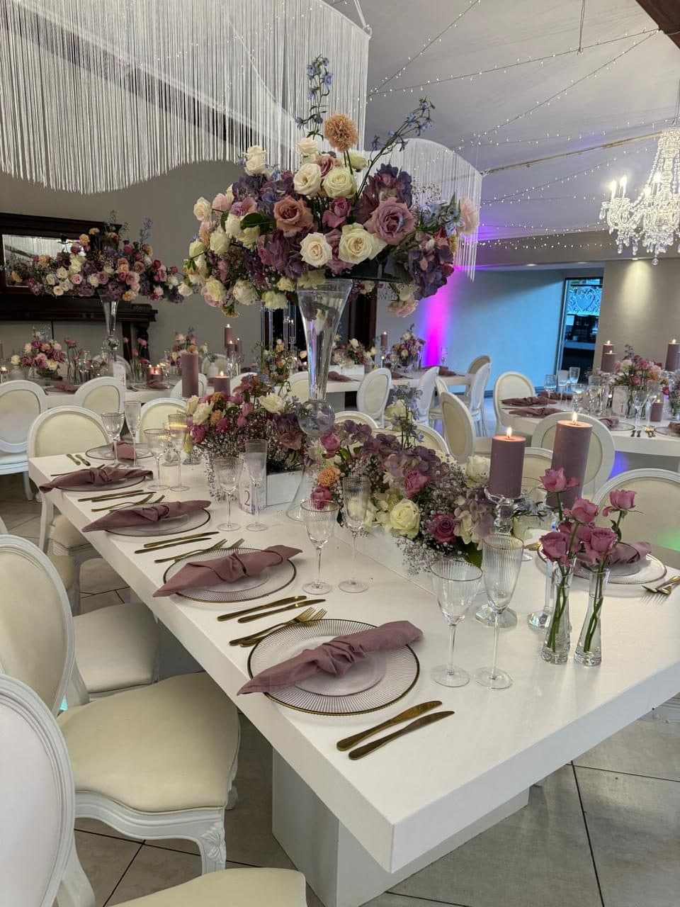 Long table set with mauve napkins, gold cutlery and tall crystal centrepieces