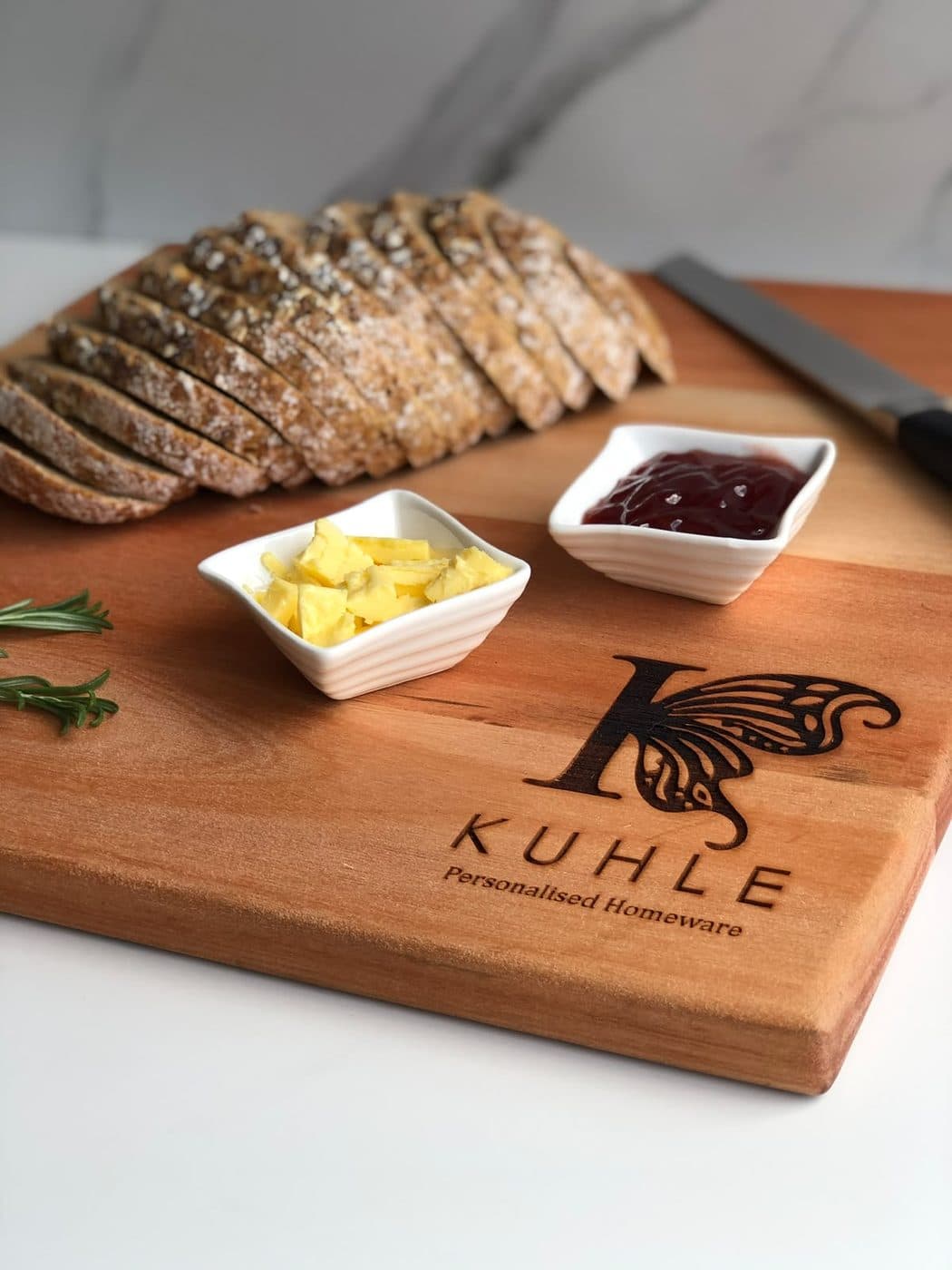 A Kuhle serving board with seeded bread, butter, preserves and fresh rosemary
