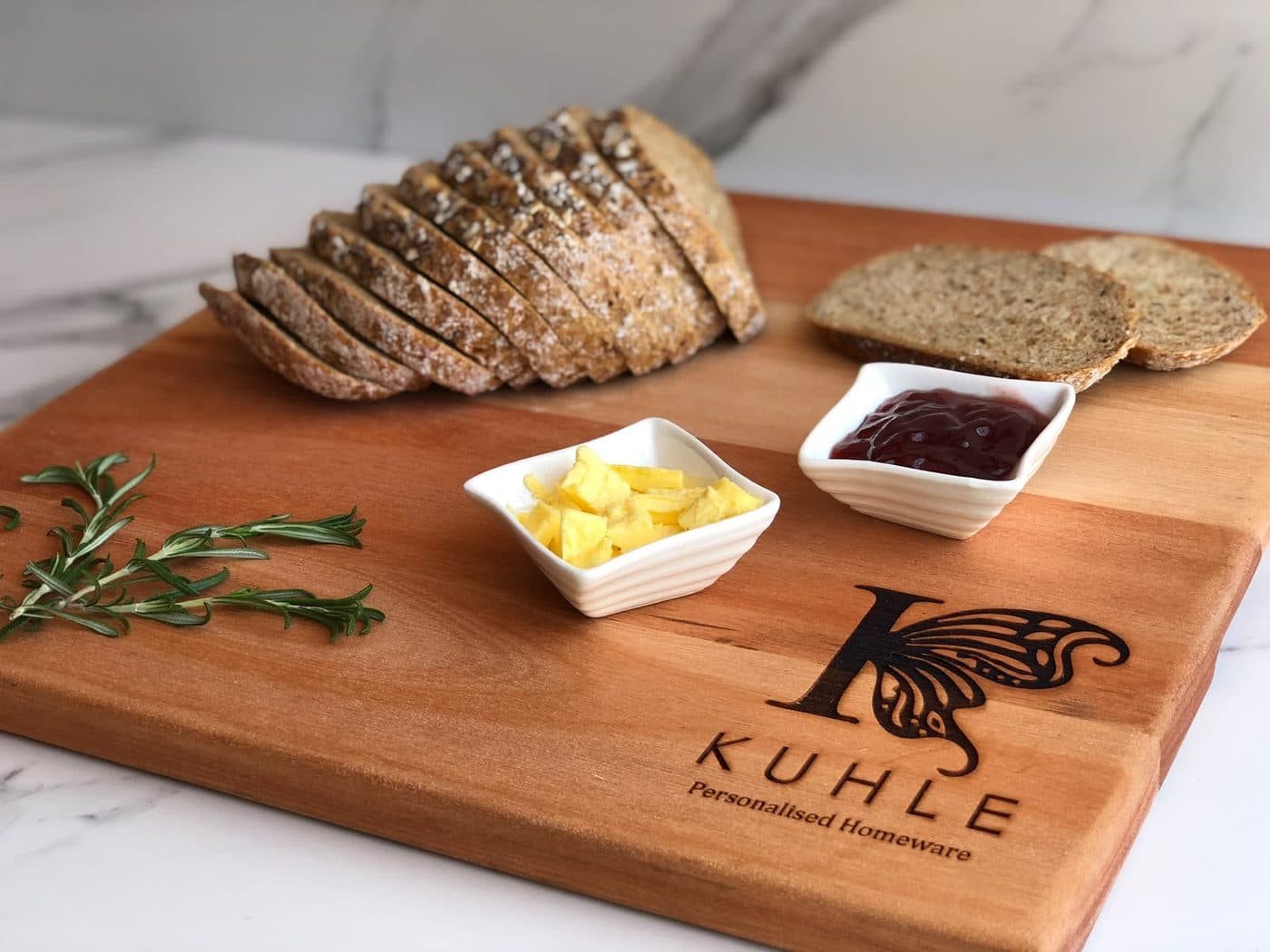 Freshly sliced bread served with butter and jam on an engraved Kuhle board