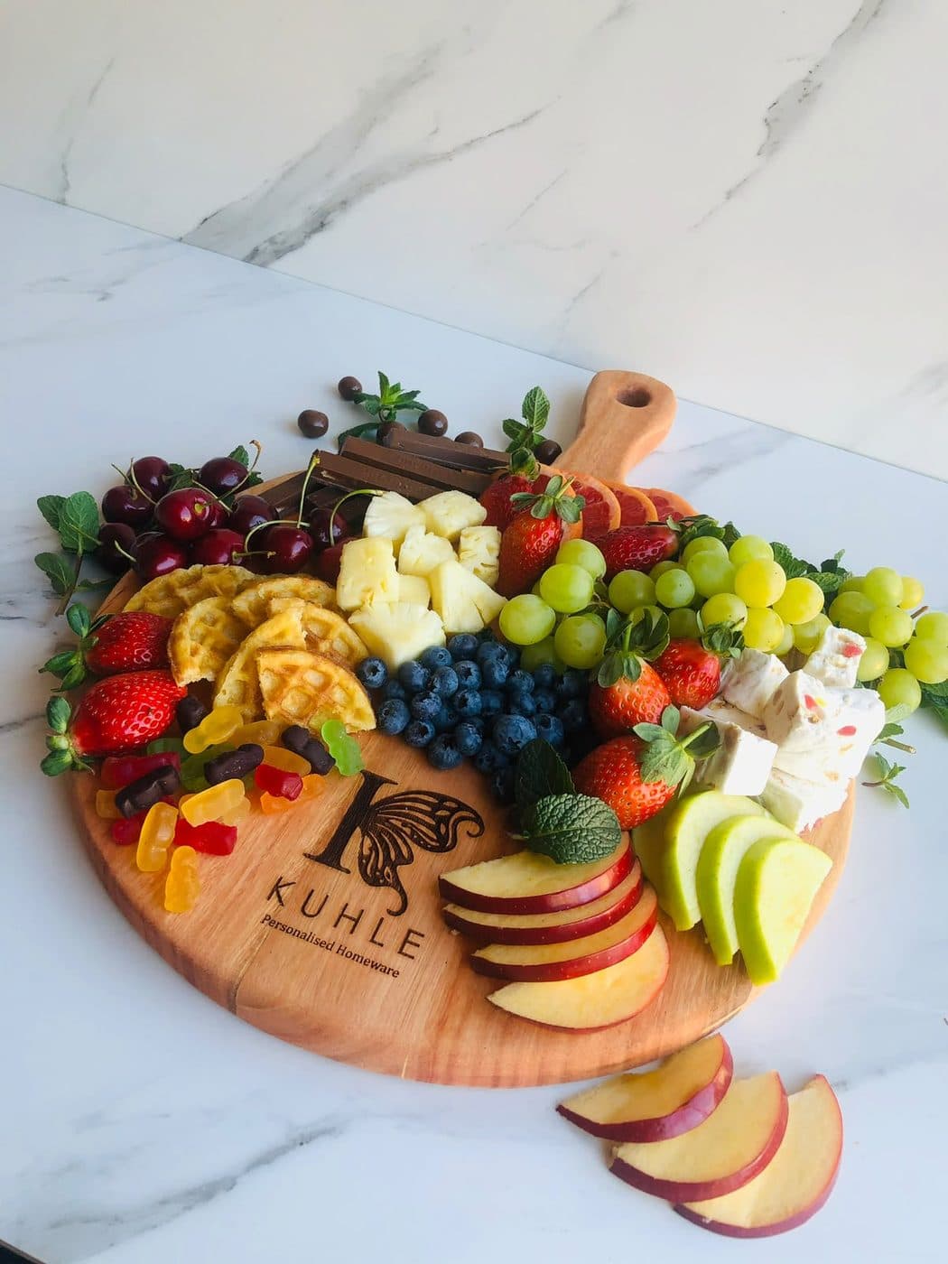 An engraved Kuhle round board dressed with berries, waffles, grapes and apple slices