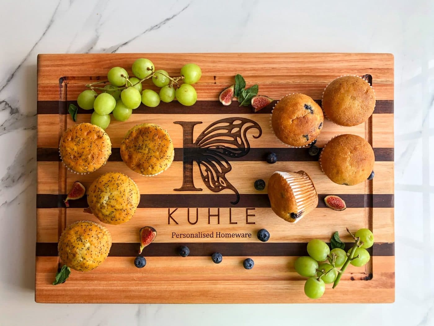 A striped mixed-wood Kuhle board arranged with muffins, figs, grapes and blueberries